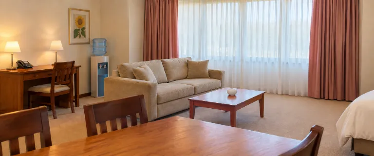 איור AI בהשראת תמונת חדר בגלריית City Mansion ApartHOTEL: חדר בגווני שמנת, ספה בז׳ אחת, שולחן עץ, וילונות ורודים וחלון מואר